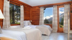 A wooden cabin room with two beds, a wooden table, and a window with curtains. - Casa del Lago Villa La Angostura (Villa La Angostura)