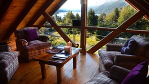 A cozy loft bedroom with a wooden ceiling and large windows offering a mountain view. - Casa del Lago Villa La Angostura (Villa La Angostura)