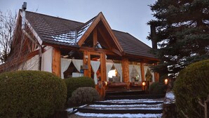 A wooden cabin with a sloped roof, a front porch, and steps leading to the entrance. - Casa del Lago Villa La Angostura (Villa La Angostura)