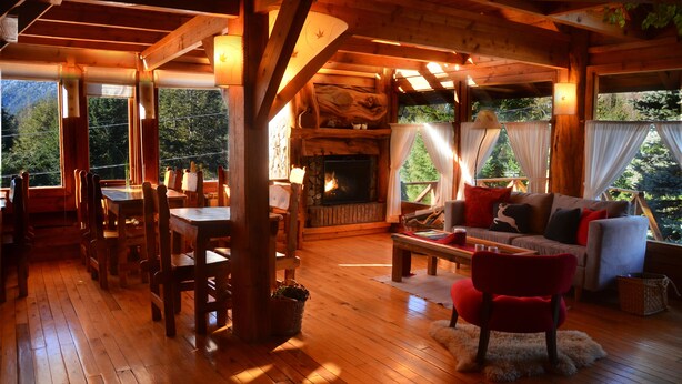 A cozy cabin interior with a wooden floor, a fireplace, a sofa, and a dining area. - Casa del Lago Villa La Angostura (Villa La Angostura)