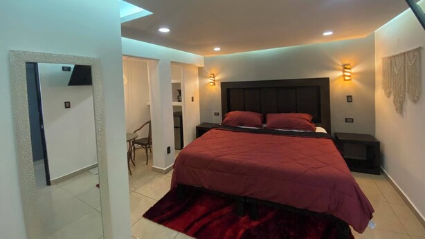 A modern bedroom with a large bed, bedside lamps, and a mirror. - Hotel Flores (Guamuchil)