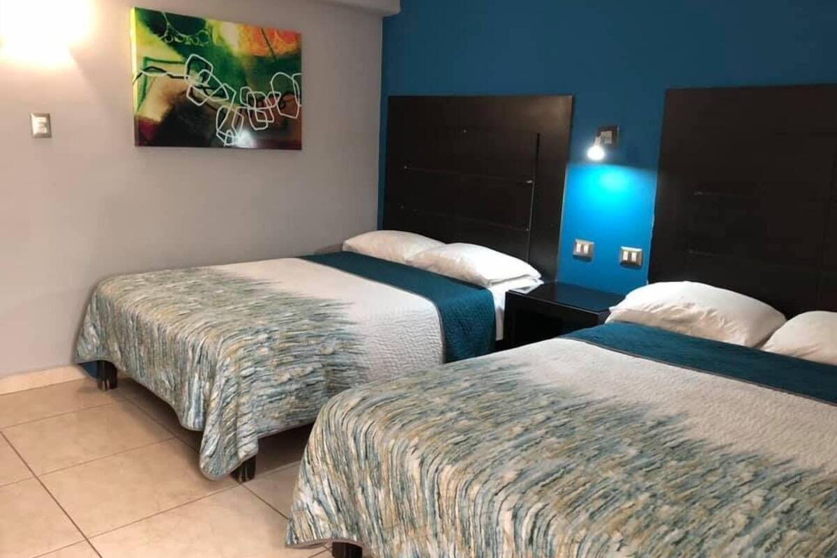 A hotel room with two beds, a large abstract painting on the wall, and a blue accent wall.