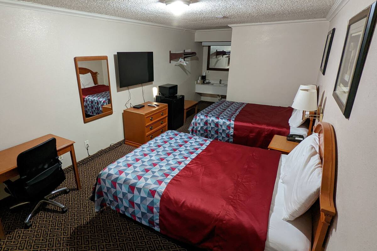 A hotel room with two beds, a desk, a chair, a TV, a dresser, and a lamp.