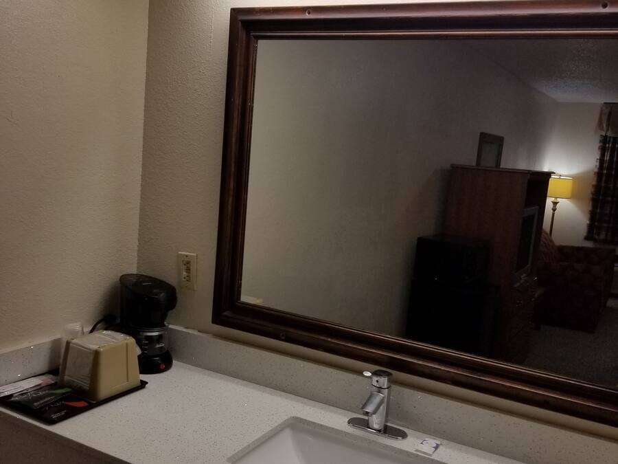 A hotel bathroom with a white sink, a large mirror, and a coffee maker.