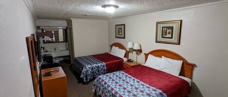 A hotel room with two beds, a desk, a mirror, and a wardrobe.
