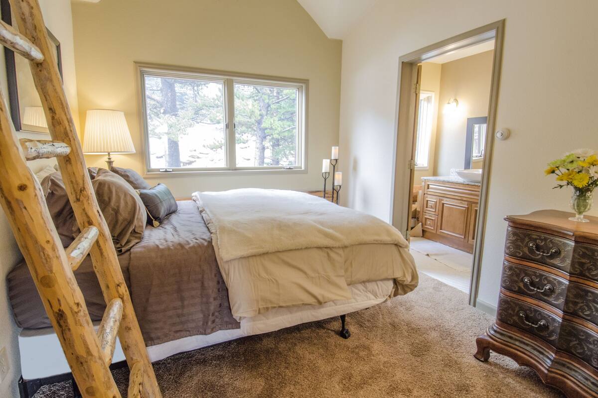 A bedroom with a bed, a wooden dresser, a mirror, a window, and a lamp.