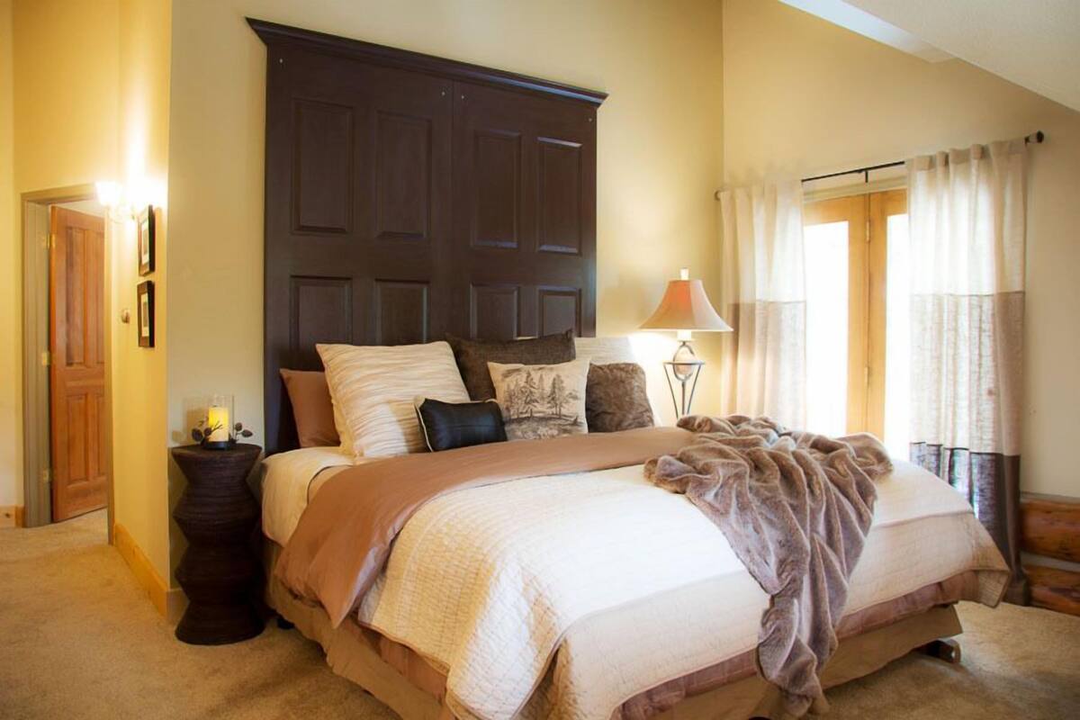 A bedroom with a large bed, a dark wooden headboard, a bedside lamp, and a window with curtains.