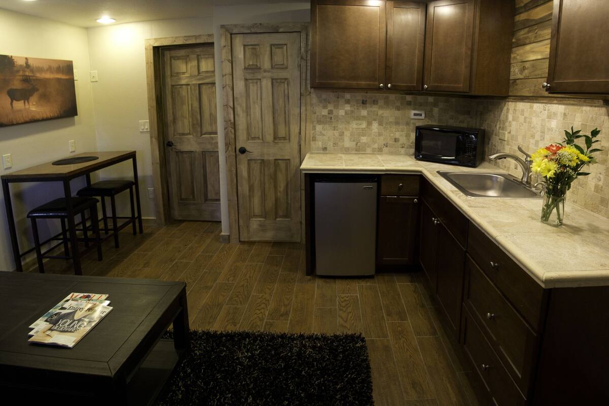 A compact kitchen with wooden cabinets, a microwave, a sink, and a dining area with a table and chairs.