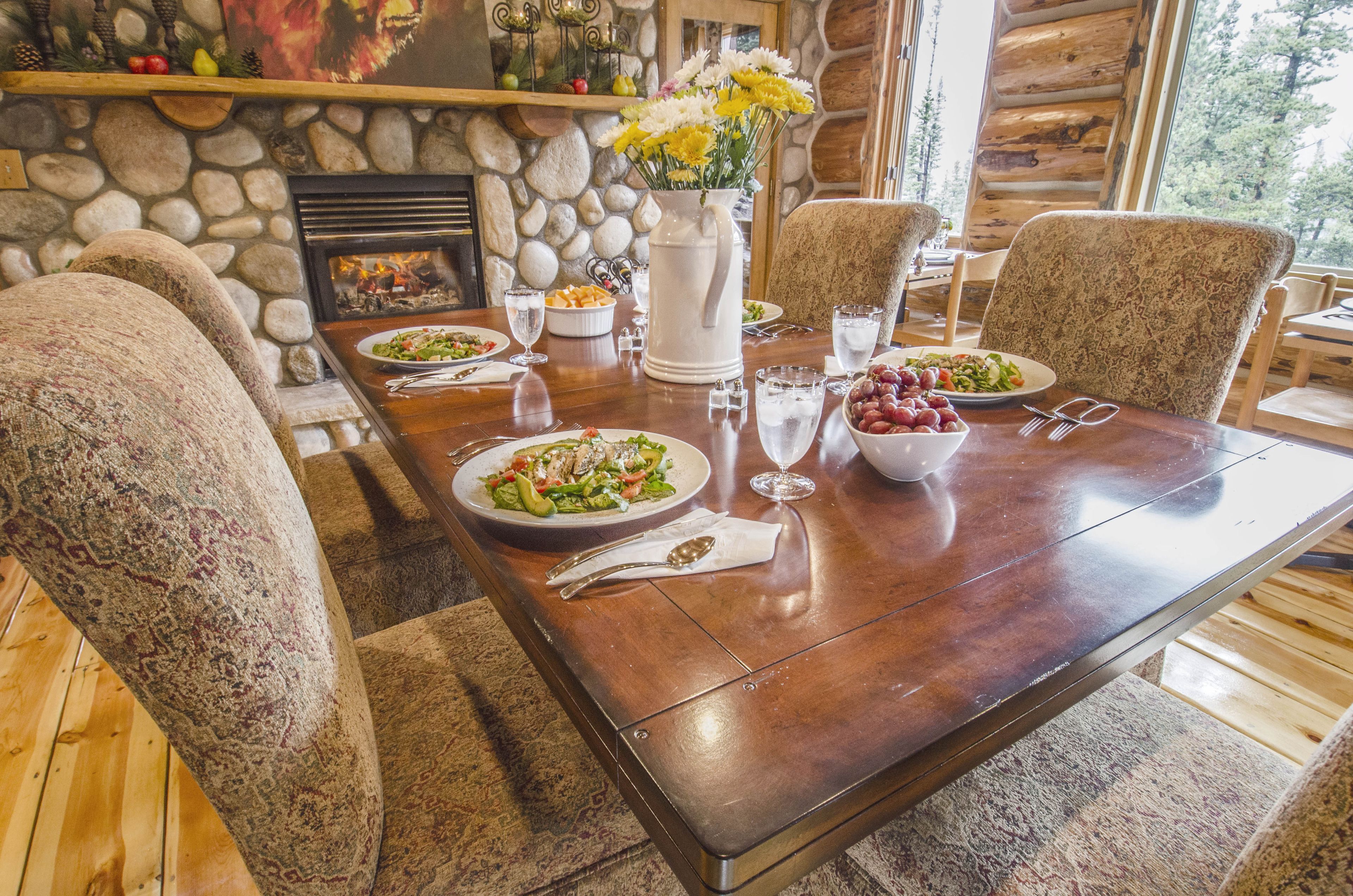 Una mesa de comedor dispuesta con platos de comida, un jarrón de flores y vasos.