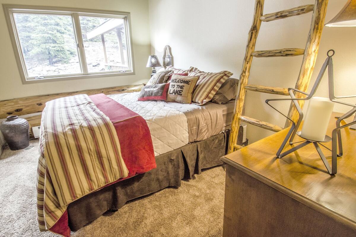 A bedroom with a bed, pillows, a desk, and a window with a view of trees.