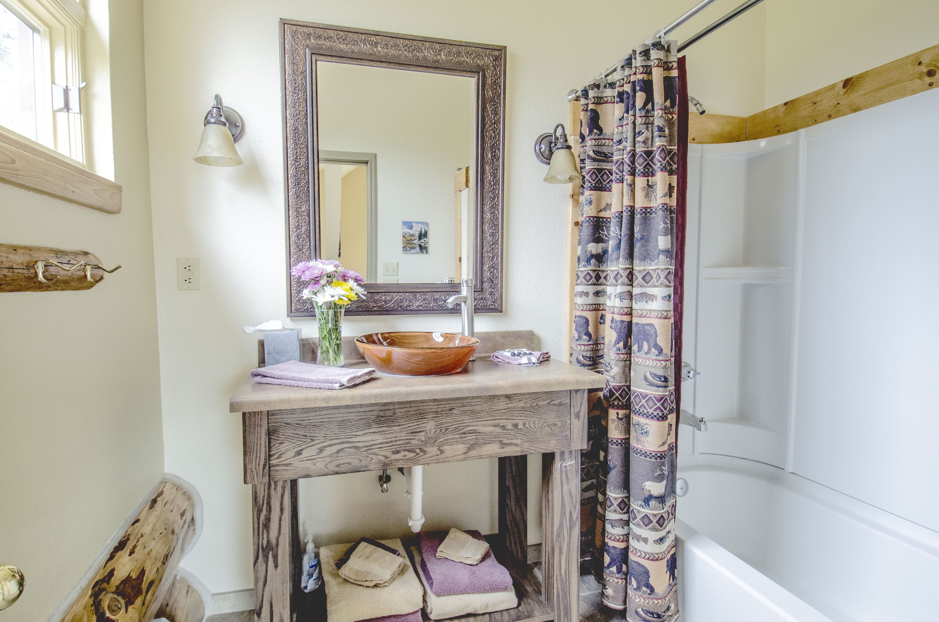 Une salle de bain avec un meuble-lavabo en bois, un grand miroir, un lavabo en forme de cuvette et un rideau de douche à motifs.