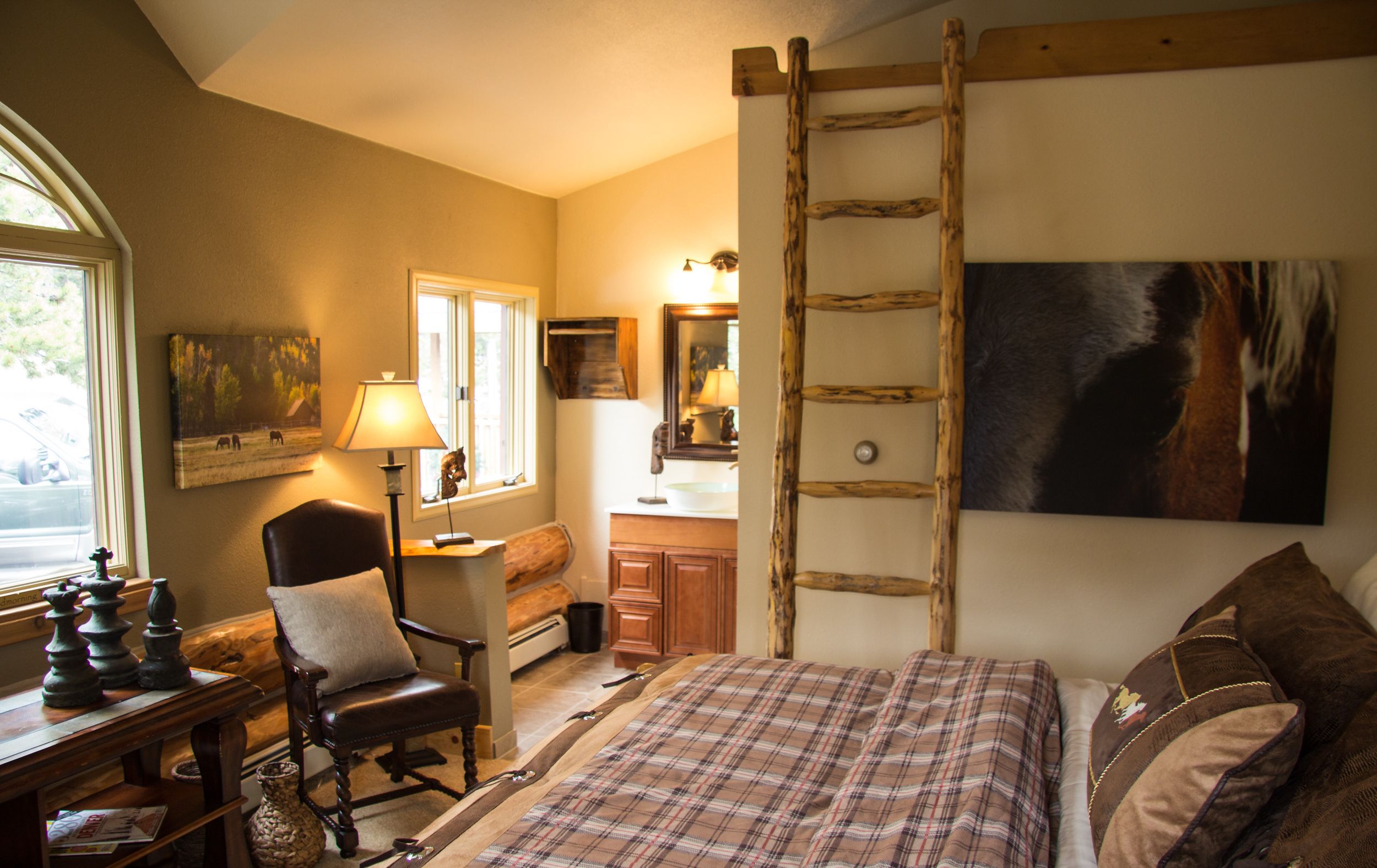 Un dormitorio con cama, una silla, un escritorio con piezas de ajedrez, una escalera, un cuadro y una ventana.