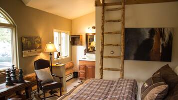 Un dormitorio con cama, una silla, un escritorio con piezas de ajedrez, una escalera, un cuadro y una ventana.