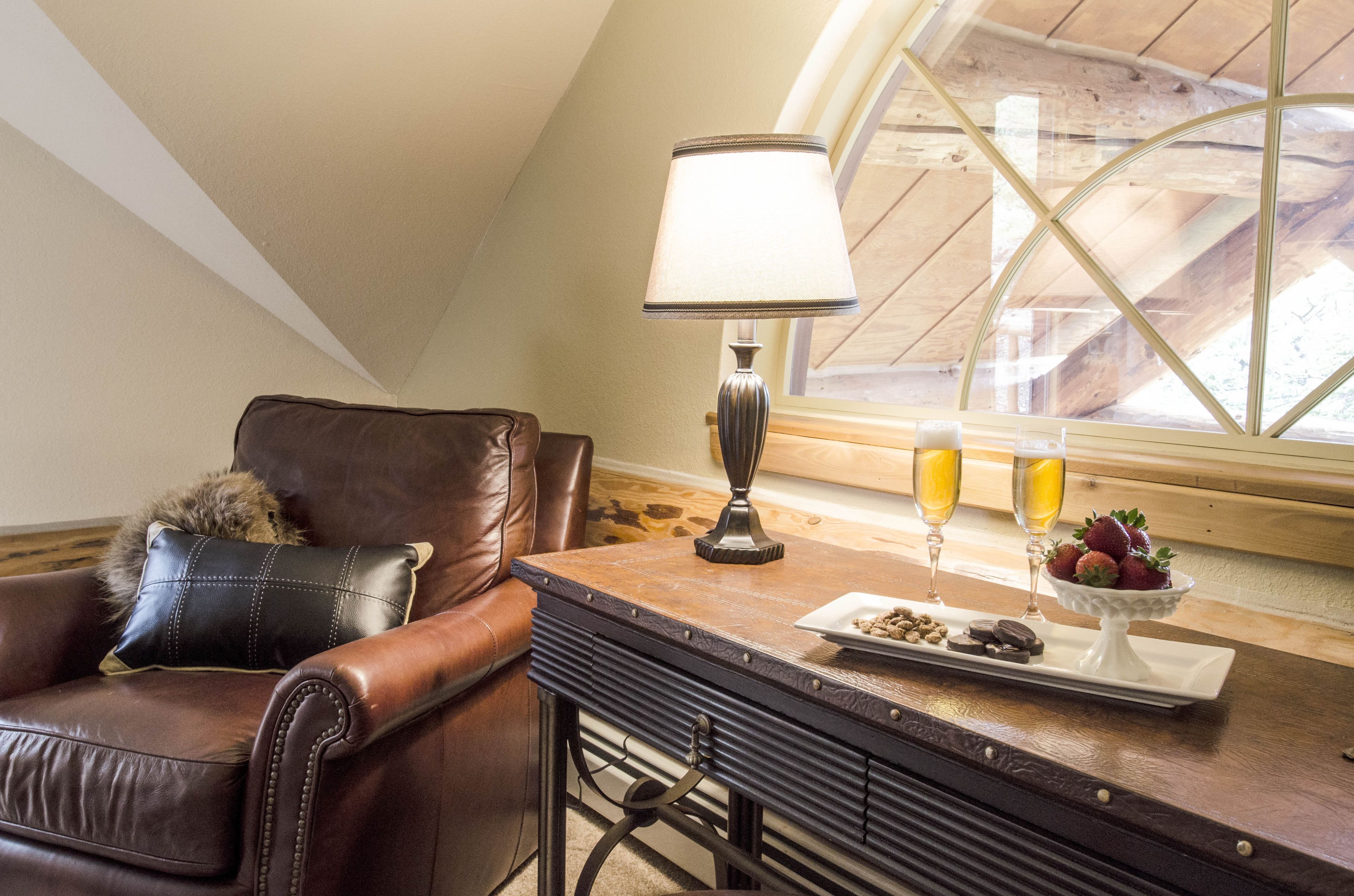 A cozy room with a leather armchair, a table with a lamp, a tray of snacks, and two glasses of orange juice.