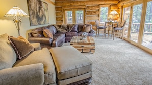 L’intérieur d’une cabane en rondins est aménagé avec un canapé d’angle en cuir, une table basse en bois et un coin repas comprenant quatre chaises.