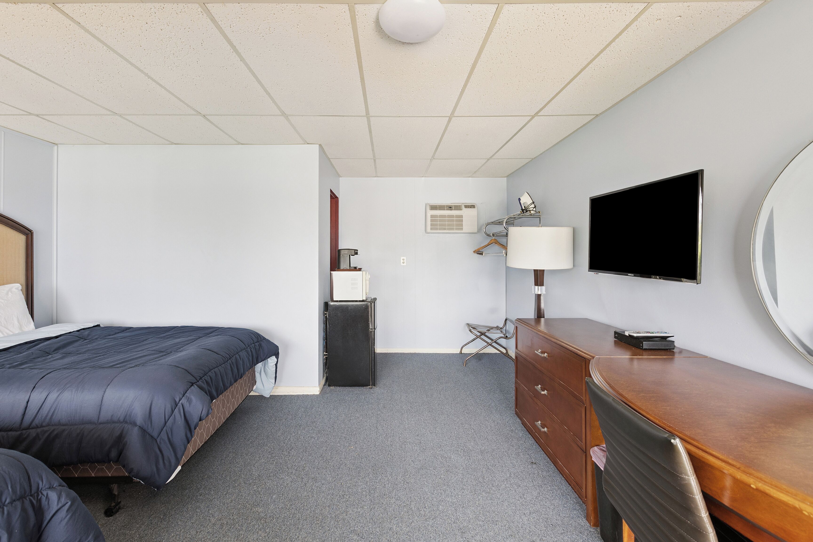 Habitación de hotel con cama, escritorio, silla, televisor, lámpara y armario.