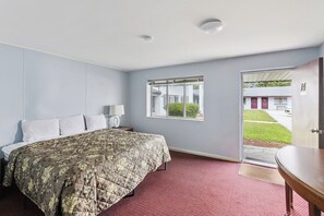 A hotel room with a bed, a nightstand, a lamp, a window, and a door leading outside. - Heidelberg Motel by Capital O Bridgeport Frankenmuth I 75 (Bridgeport)