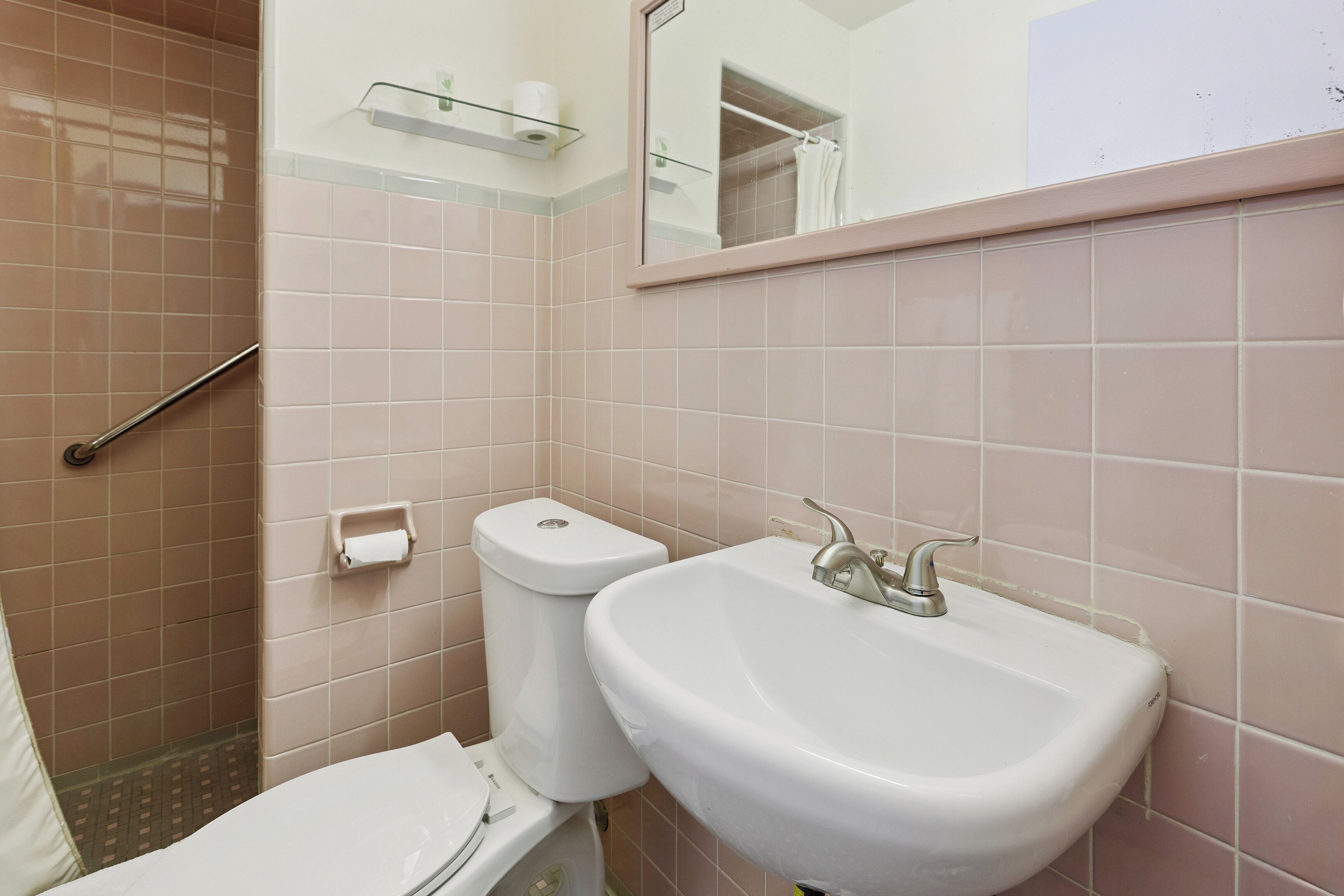 Een badkamer met een toilet, wastafel en een glazen plank boven het toilet.