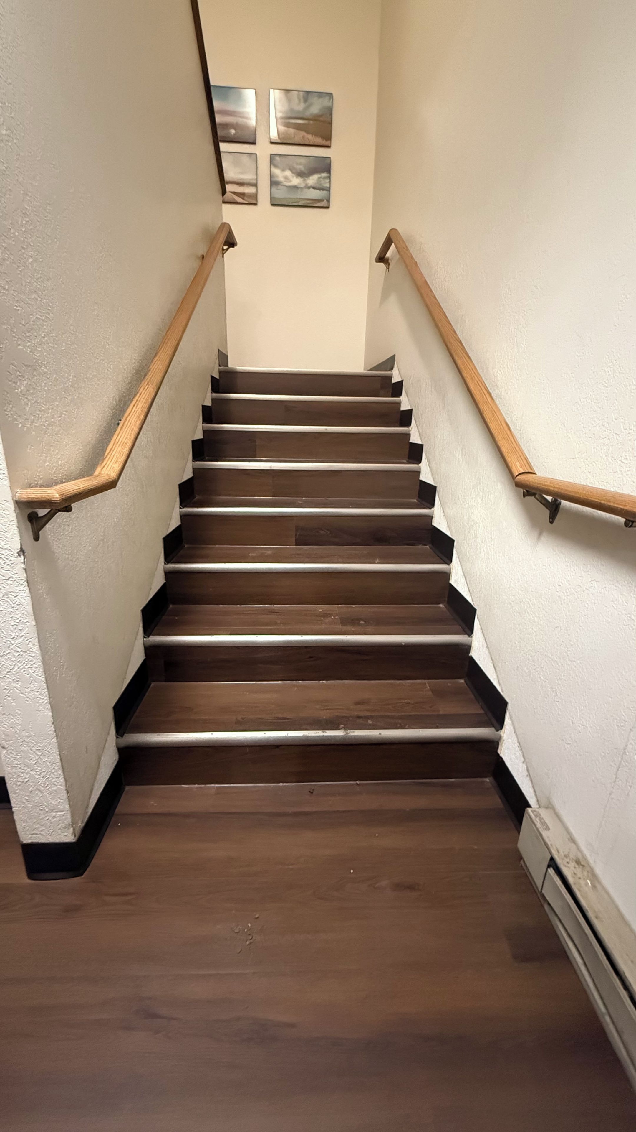 A wooden staircase with a handrail on both sides, leading to a landing with four framed pictures.