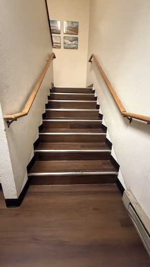 A wooden staircase with a handrail on both sides, leading to a landing with four framed pictures.