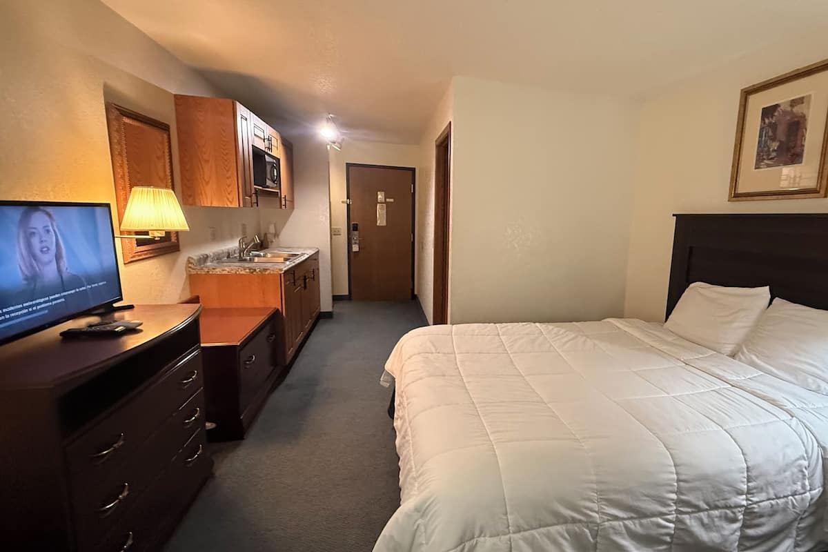 Quarto de hotel com uma cama, televisão, escrivaninha, abajur e porta para um banheiro.