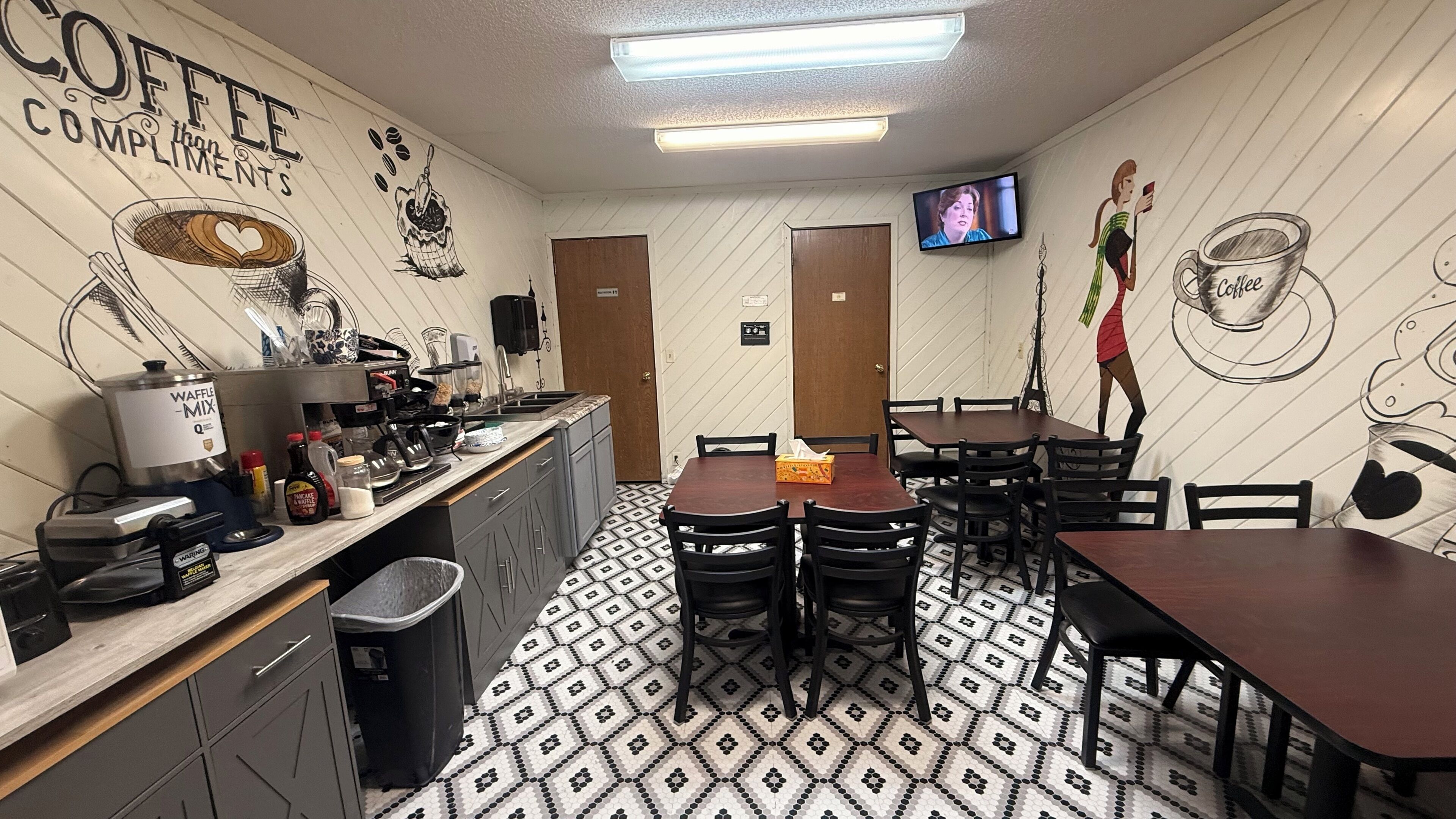 Una cafetería con mostrador, mesas, sillas, un televisor y piso estampado.