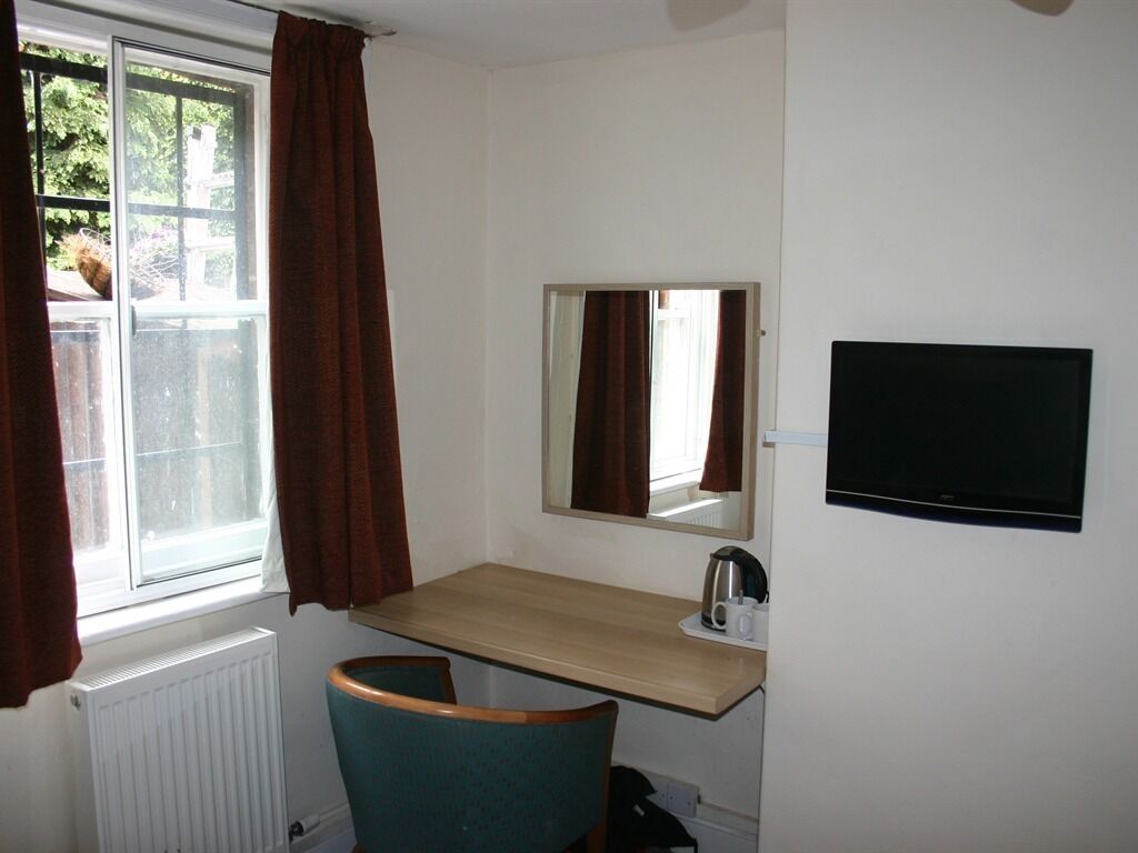 A small room with a window, a mirror, a television, a wooden desk, and a chair.