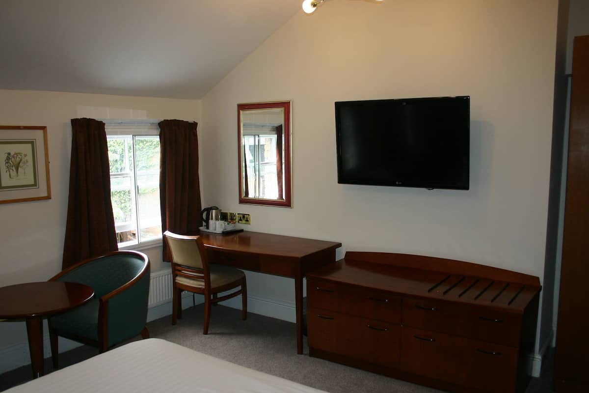 Quarto de hotel com cama, escrivaninha, cadeira, cômoda, televisão e janela com cortinas.