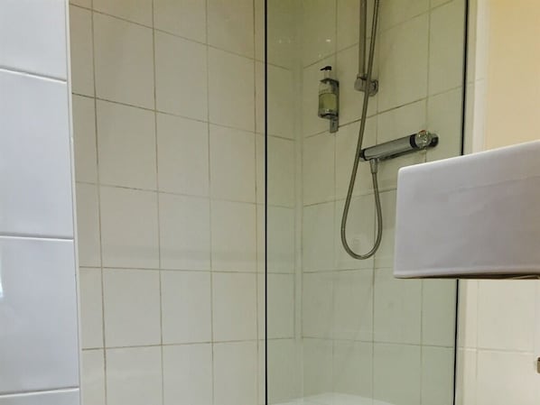 Ducha con puerta de vidrio, cabezal de ducha de mano y dispensador de jabón.