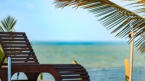 A wooden lounge chair with a metal pole, positioned near a palm tree and ocean view.
