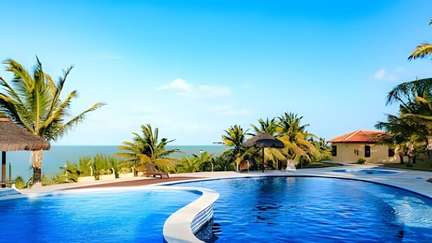 A swimming pool with a curved edge, surrounded by palm trees and a building with a red roof.