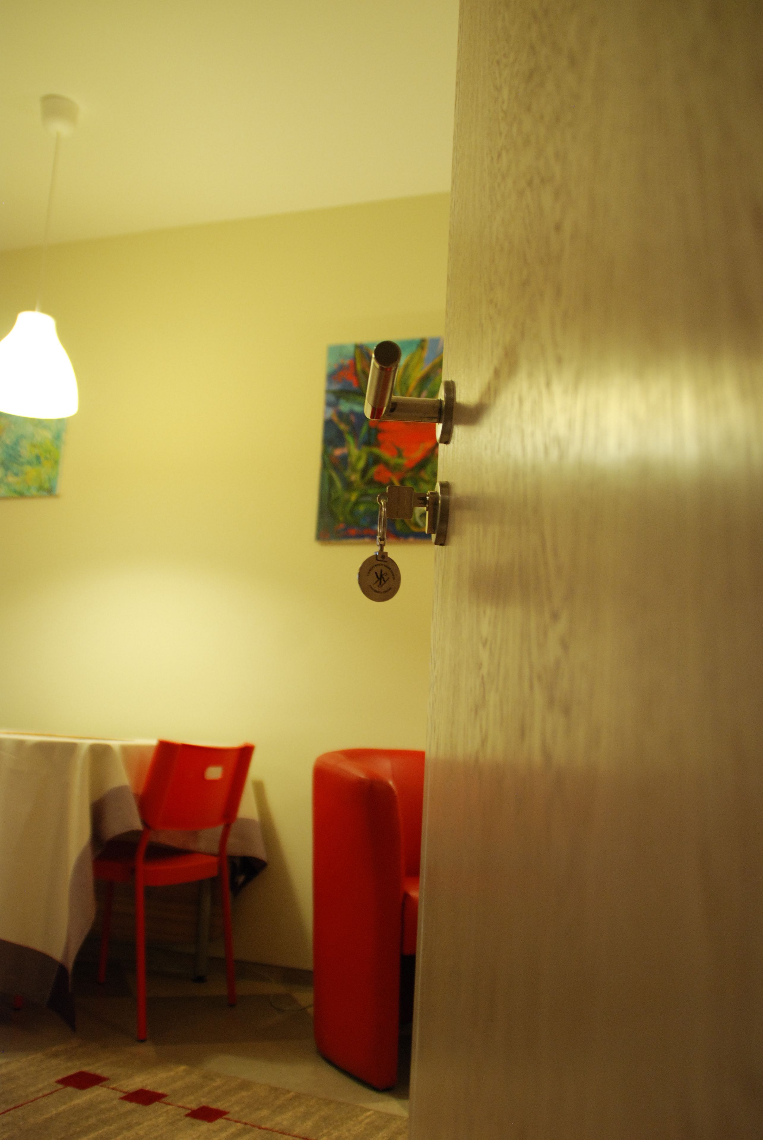 A room with a table and chairs, a painting on the wall, and a door with a lock.