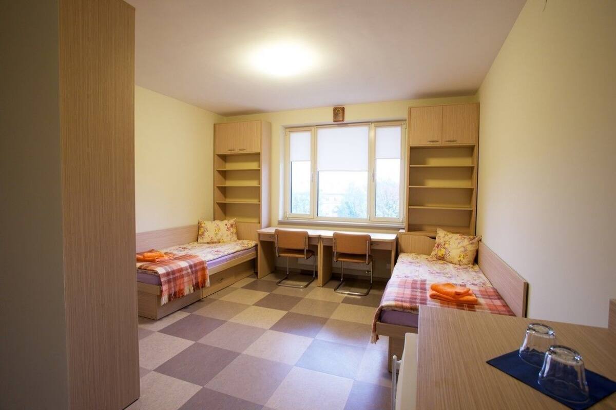 Une chambre de dortoir avec deux lits, un bureau et une fenêtre.