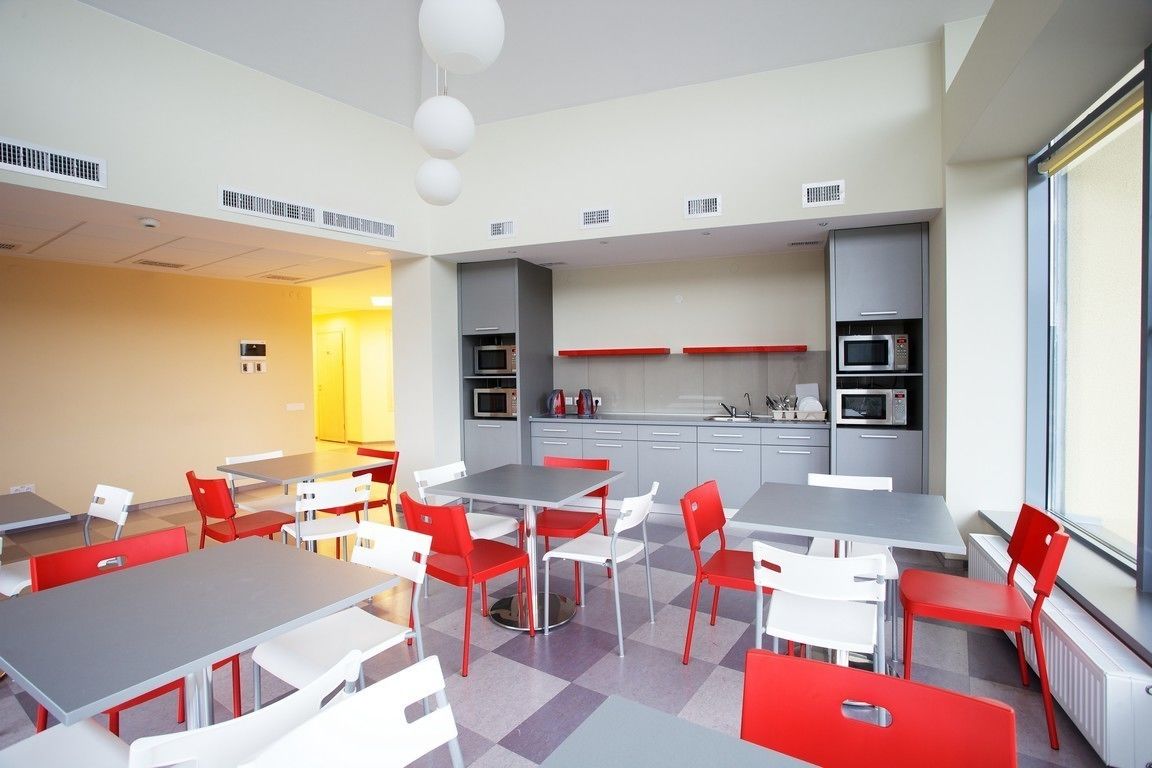 Un comedor moderno con mesas y sillas, una cocina al fondo y un ventanal con vistas.