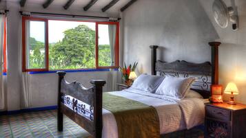 Une chambre à coucher comprenant un lit, une table de chevet, une lampe, une fenêtre avec des rideaux et une vue sur la verdure à l’extérieur.