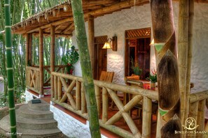 Een traditionele bamboestructuur met een stenen fundering, houten leuningen en een zithoek met tafels en stoelen.