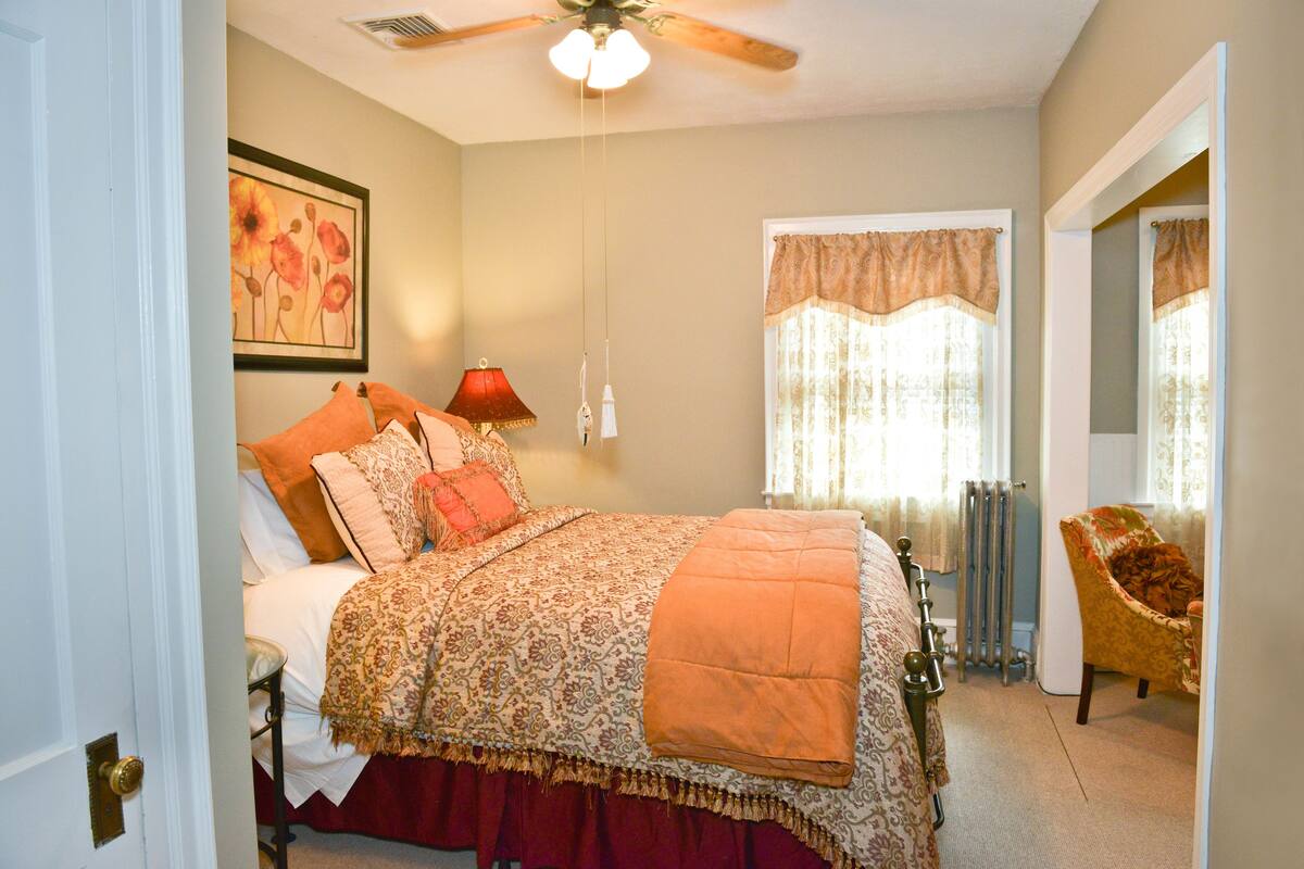 A bedroom with a bed, a chair, a radiator, and a ceiling fan.
