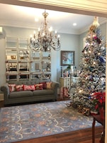 Una sala de estar acogedora con un sofá gris, una araña, un árbol de Navidad y una alfombra estampada.