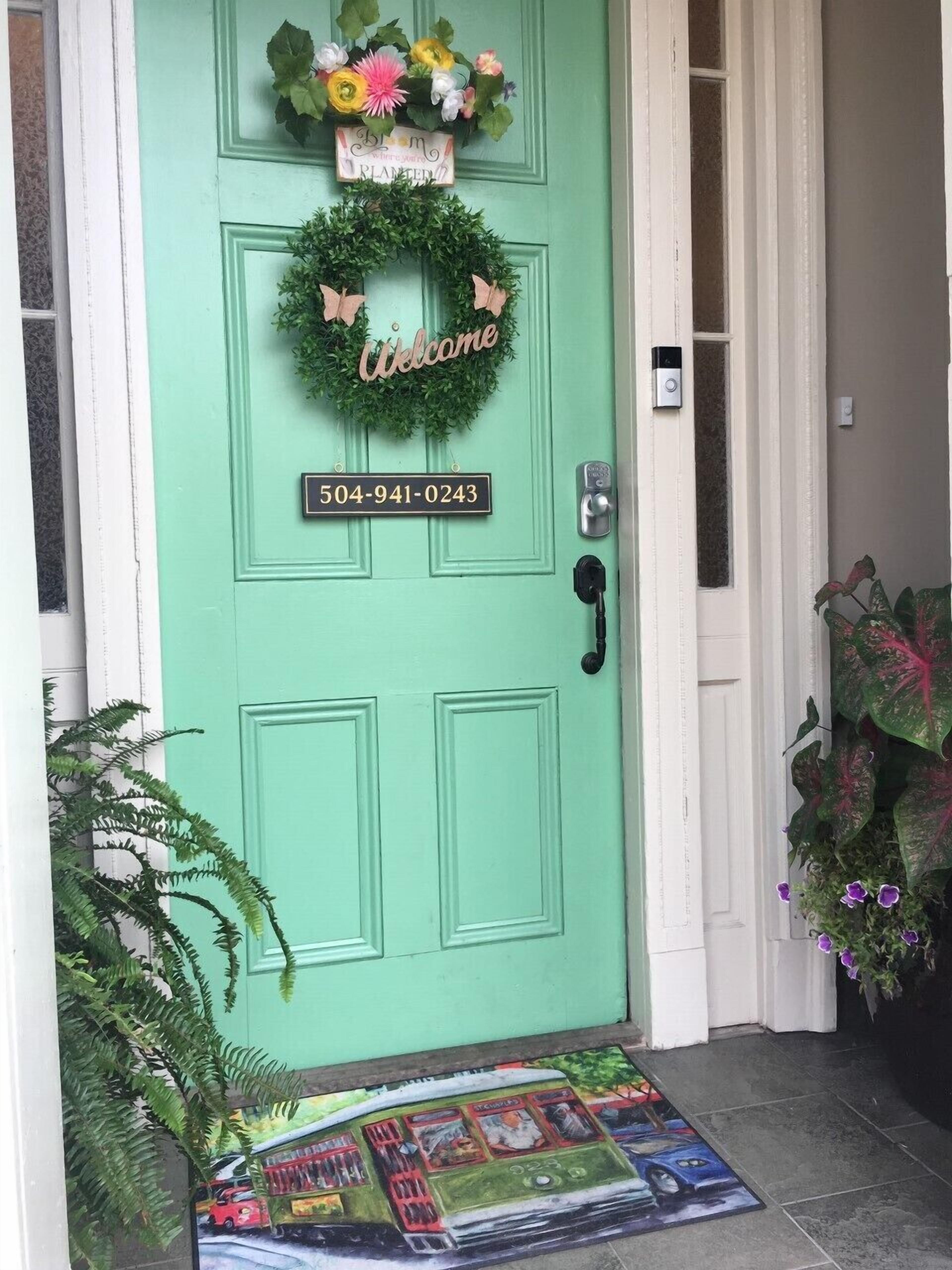 A teal door with a welcome wreath, a doorbell, and a number plate.
