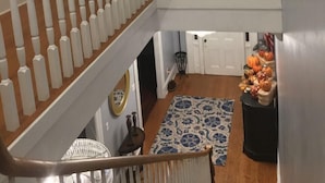 A multi-level interior with a wooden staircase, white railings, and a patterned rug.