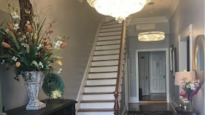 A staircase with a chandelier, a decorative vase with flowers, and a patterned rug.