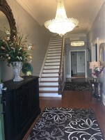 Una escalera con un candelabro, un jarrón decorativo con flores y una alfombra estampada.