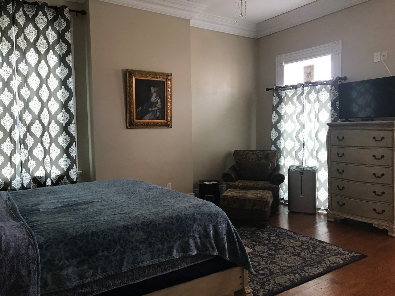 Um quarto com uma cama, uma cadeira, uma cômoda e um quadro na parede.