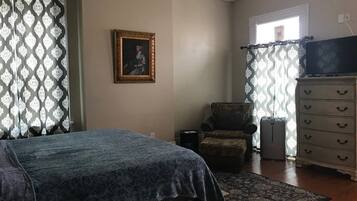 Um quarto com uma cama, uma cadeira, uma cômoda e um quadro na parede.