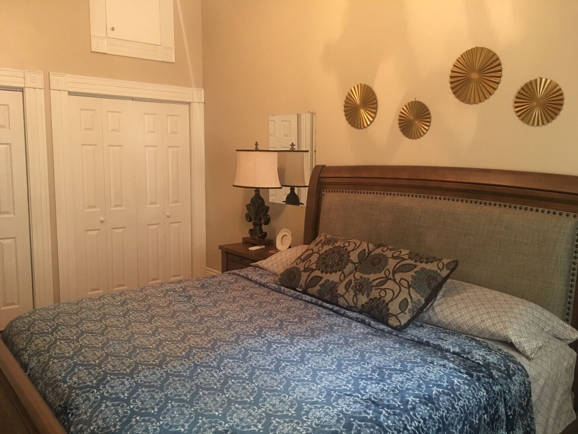 A bedroom with a bed, a nightstand, a lamp, a wall clock, and decorative wall art.