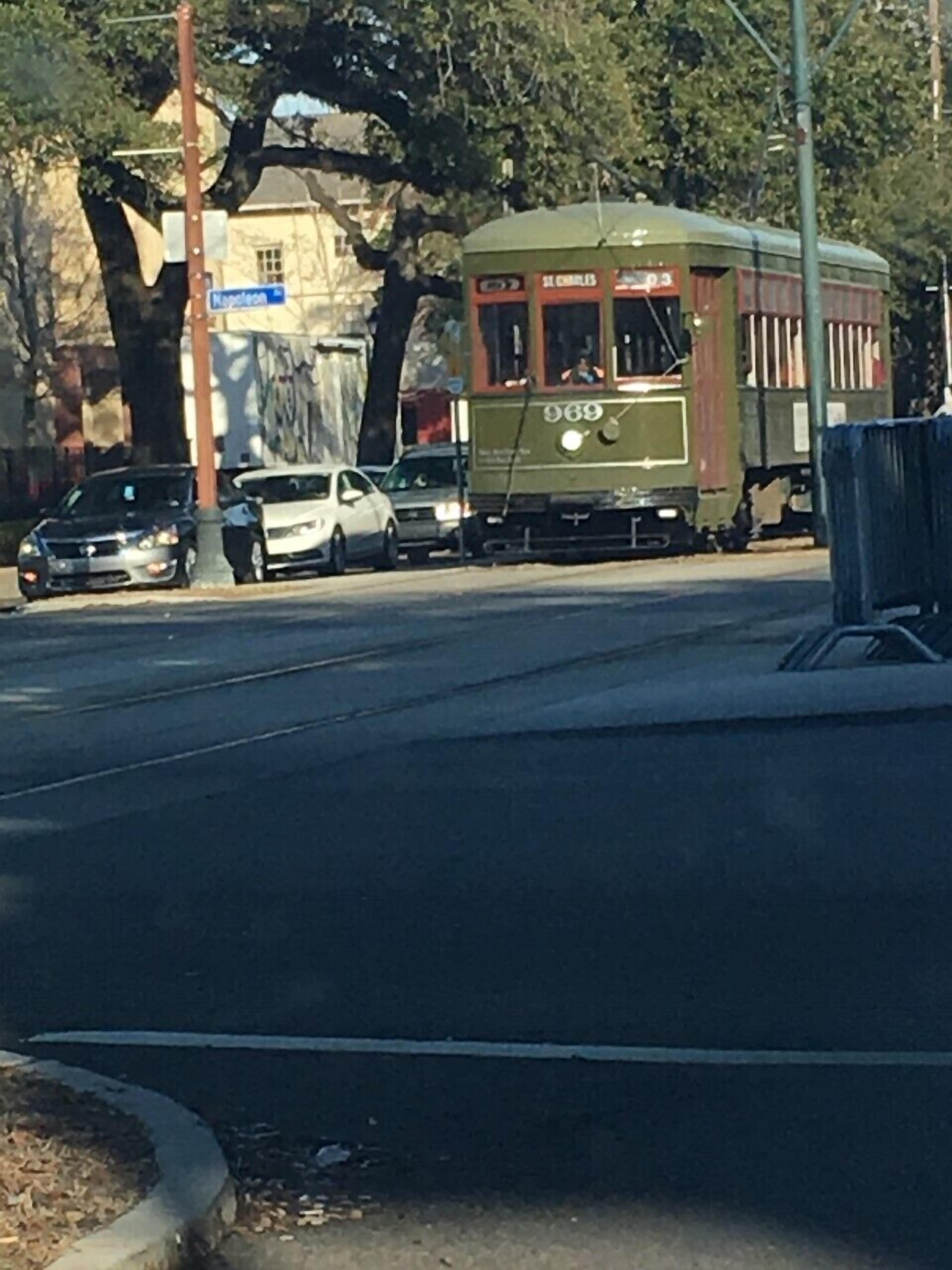 Un tram percorre una strada con auto parcheggiate lungo il lato.
