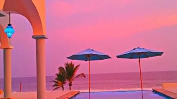 Vista de la piscina con dos sombrillas y una palmera.