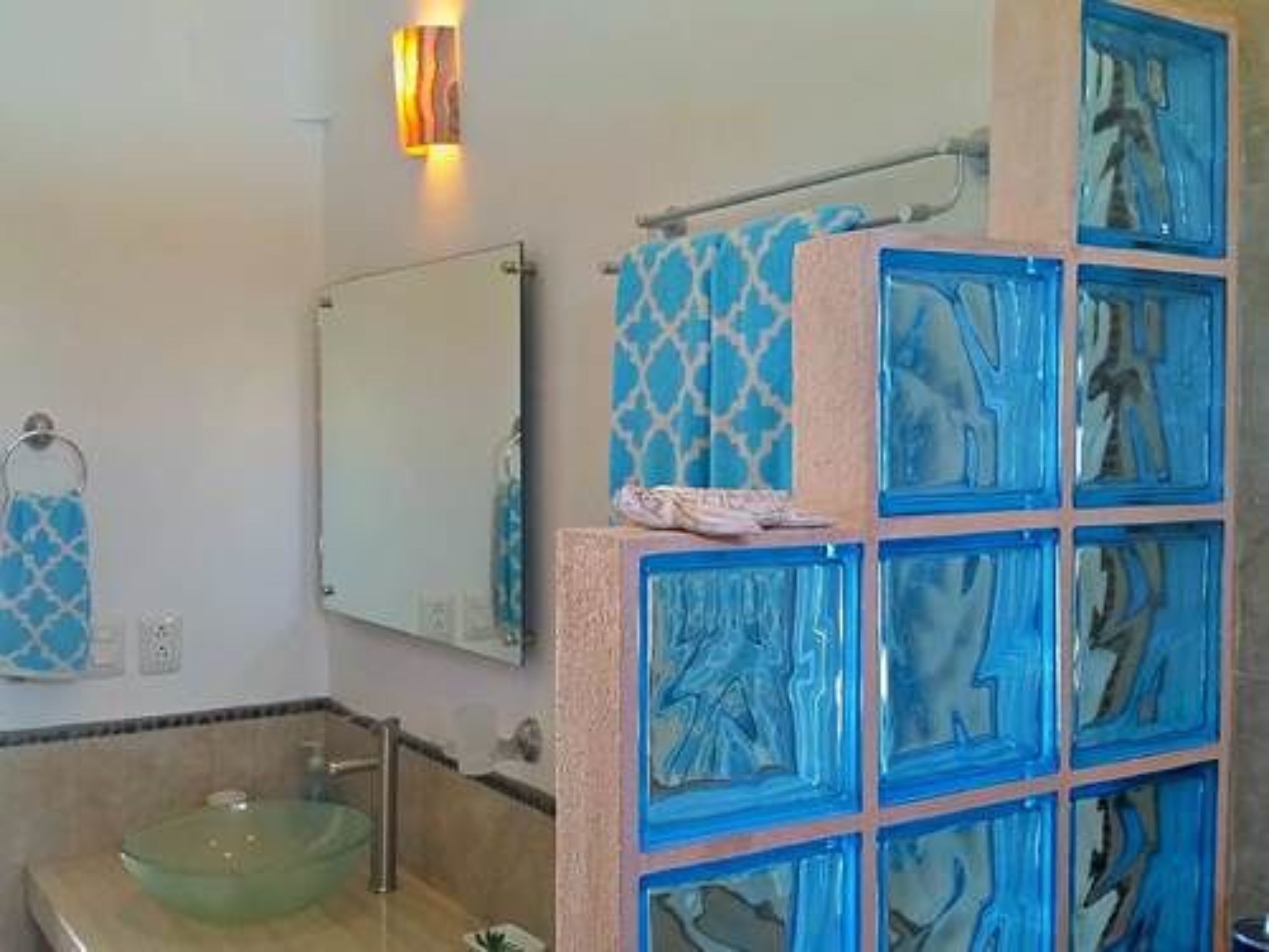 Un baño con lavamanos de vidrio, un perchero y un espejo.