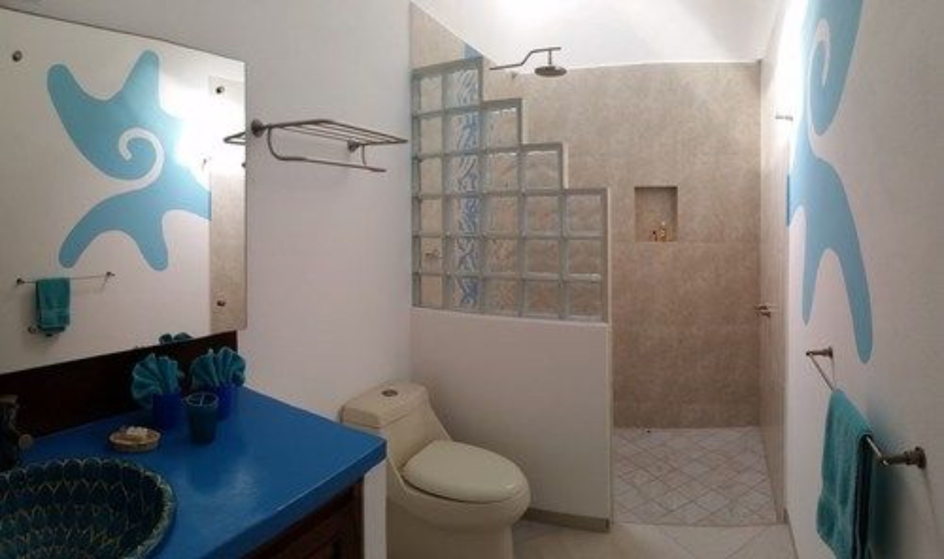 Un baño con encimera azul, inodoro, ducha con puerta de vidrio y espejo con diseño azul.