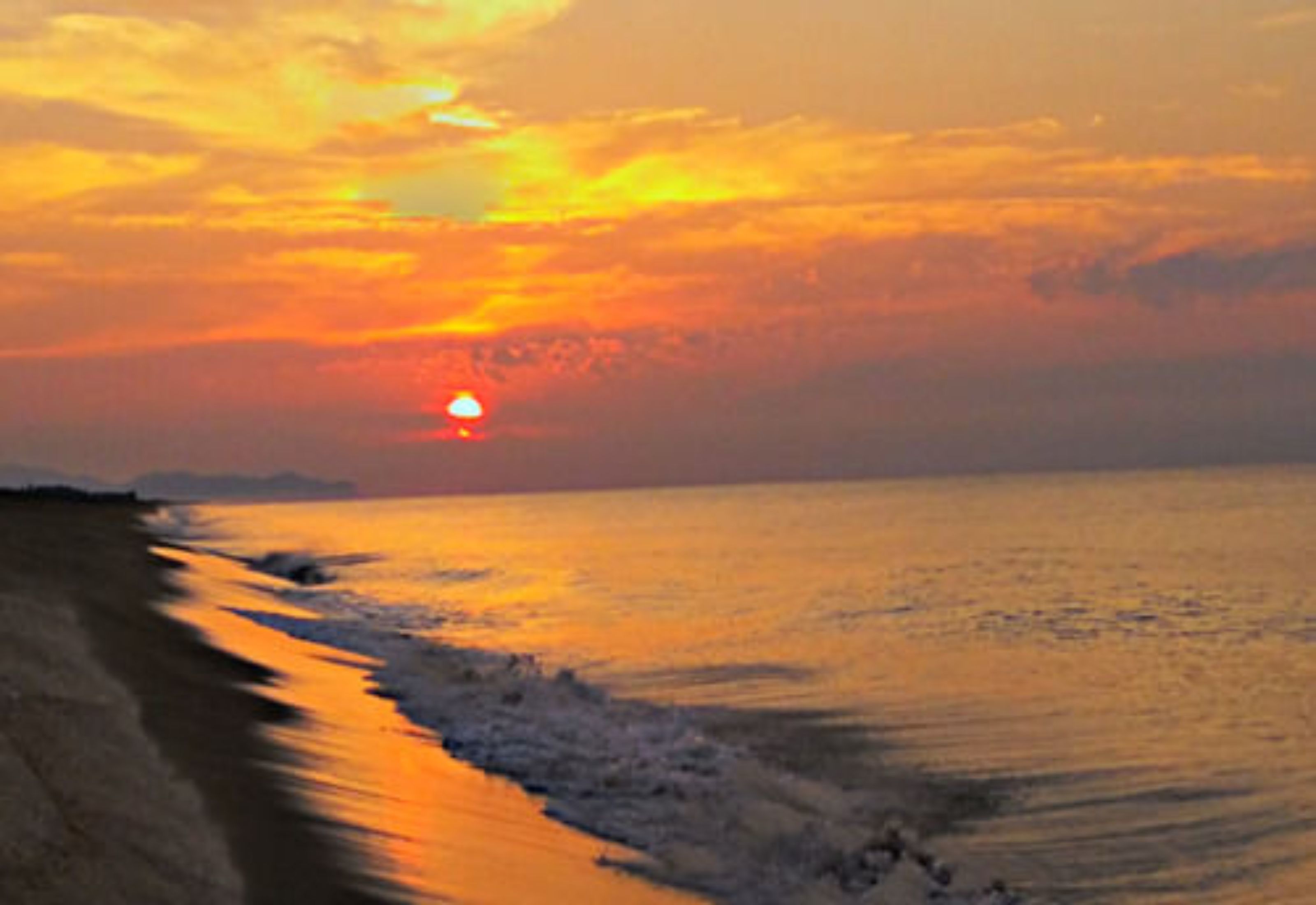 Atardecer sobre una playa, con el sol cercano al horizonte.